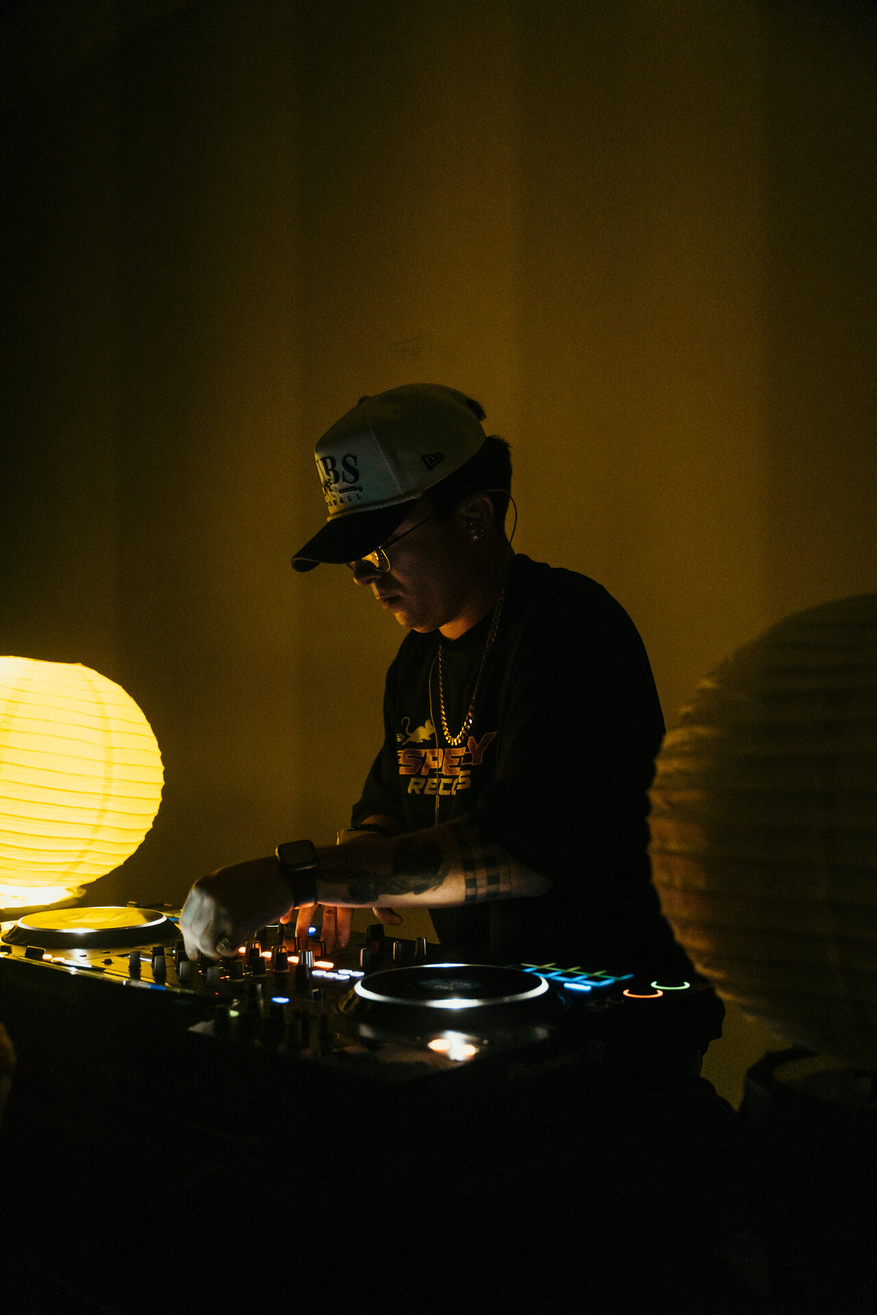 A DJ at the decks between glowing paper lanterns