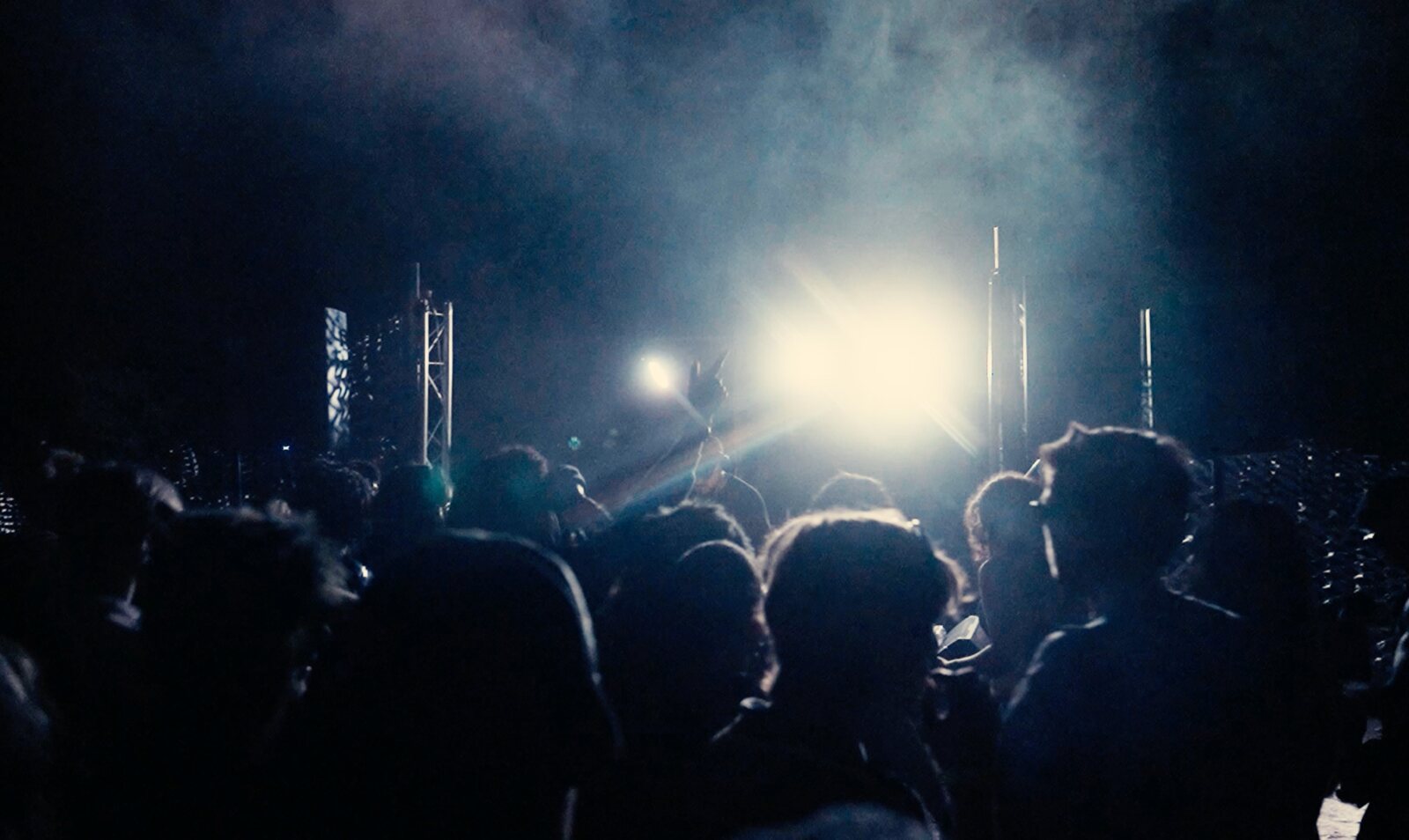 A crowd facing the stage as a bright light cuts through haze