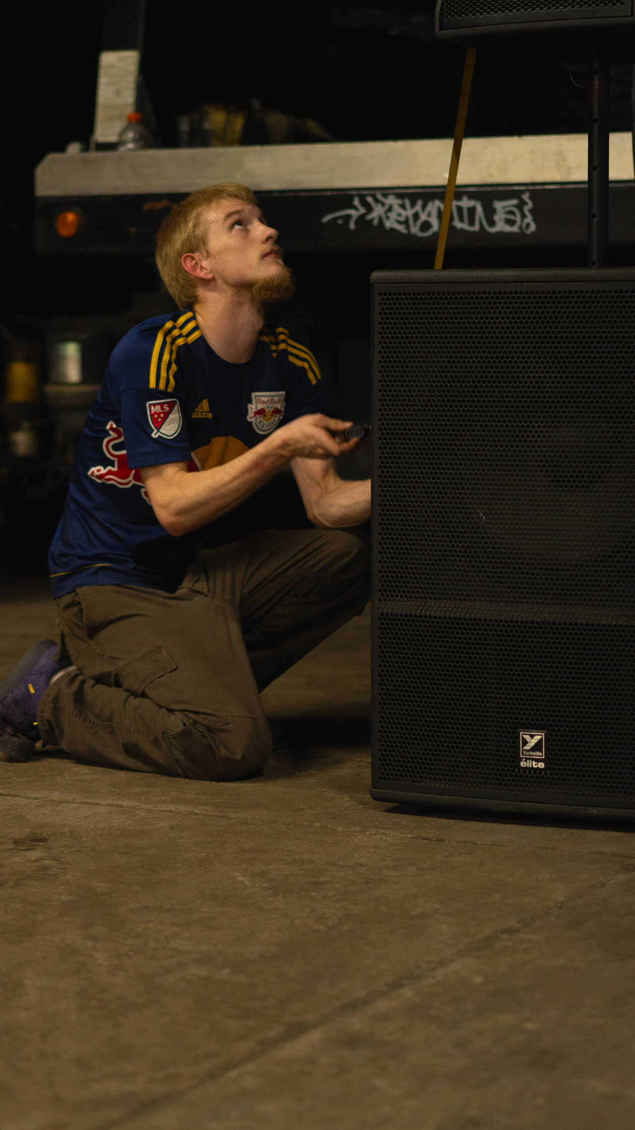 A crew member kneeling beside a powered speaker during load-in